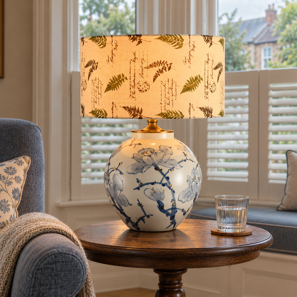 Blue and white lotus ceramic lamp with leaf-print shade beside a living room chair