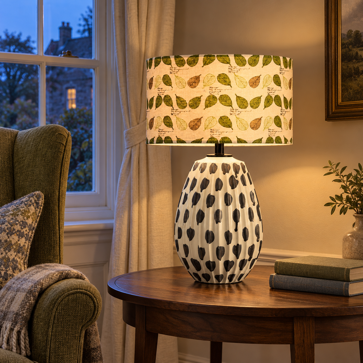 Black spot ceramic table lamp with leafy shade beside a living room chair