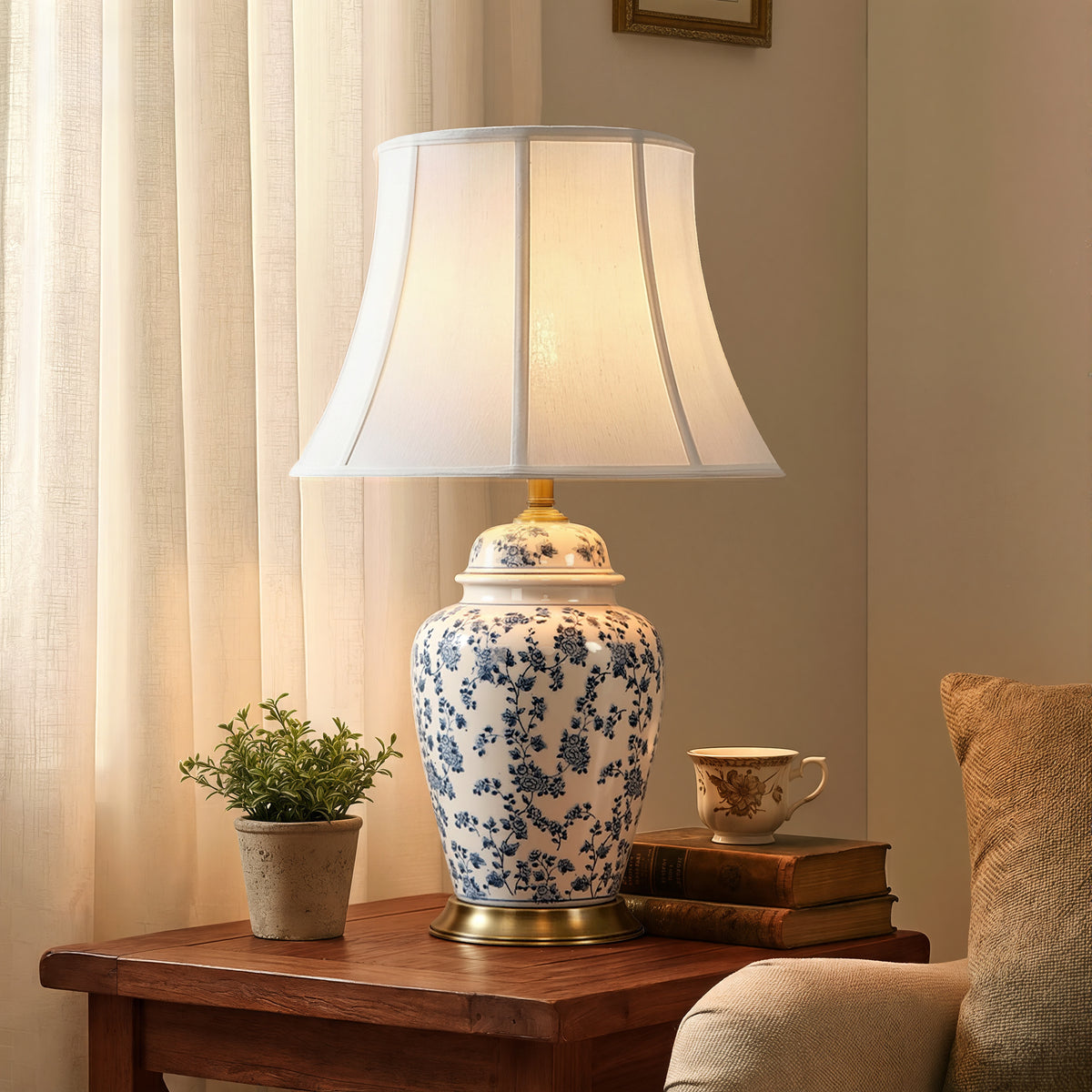 blue floral ceramic table lamp glowing beside a cream sofa and curtains