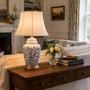 blue floral ceramic table lamp on a dark console beside sofa and flowers
